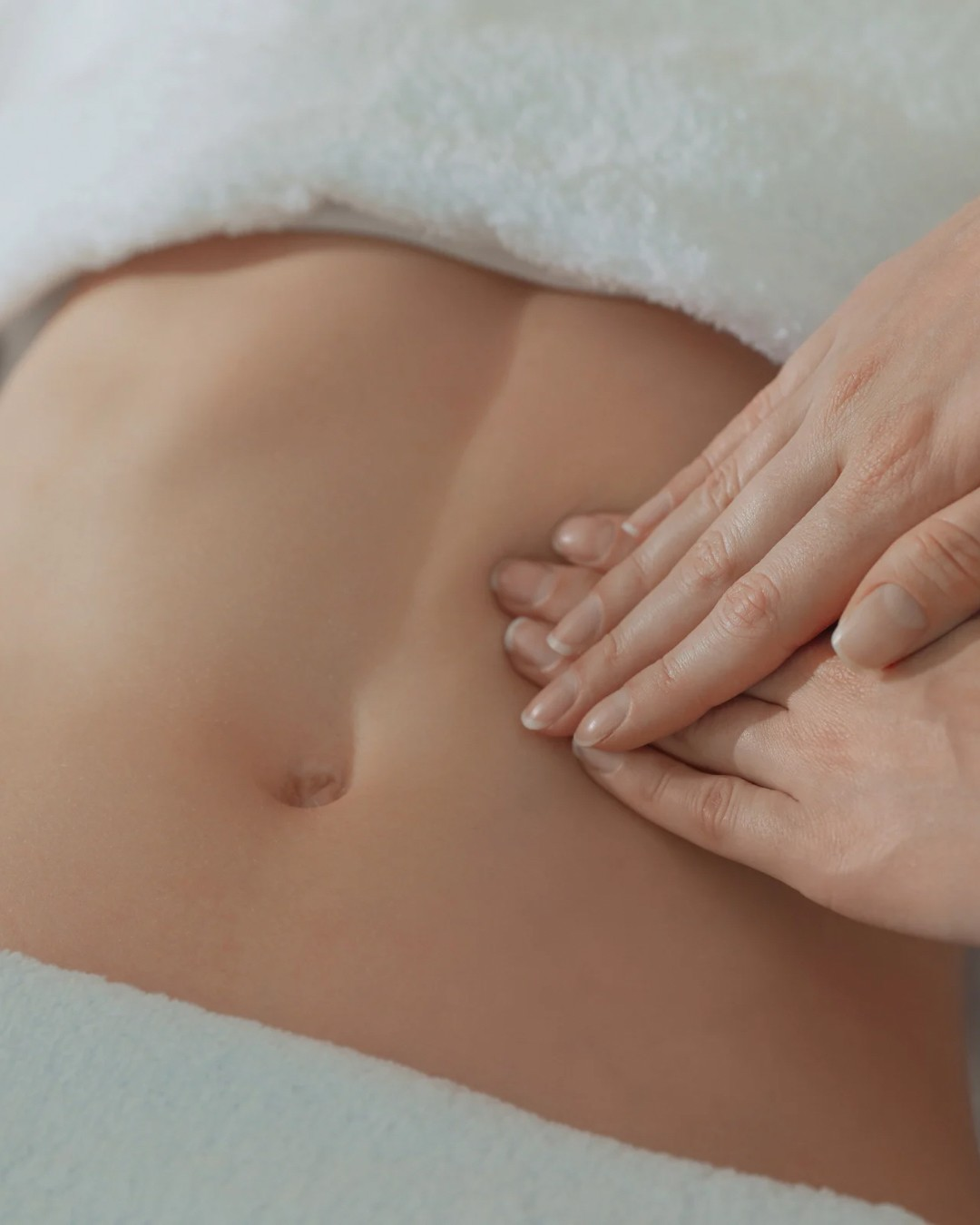 Therapist's hands performing gentle lymphatic drainage massage on a client's abdomen